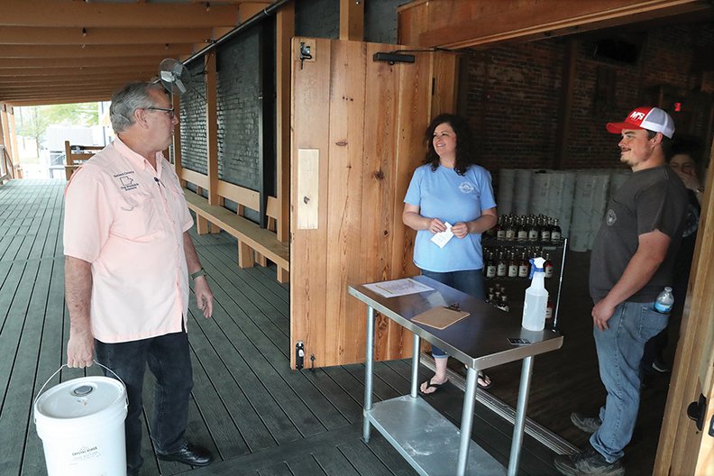 Garland County Treasurer Tim Stockdale, left, talks with co-owner Mary Bradley and employee Marshall Bean after purchasing a 5-gallon container of Crystal Ridge Distillery's hand sanitizer for the county on Friday. - Photo by Richard Rasmussen of The Sentinel-Record