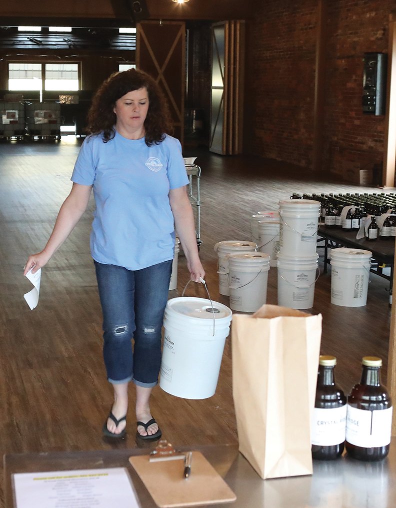 Co-owner Mary Bradley carries a 5-gallon container of Crystal Ridge Distillery's hand sanitizer out to a customer on Friday. - Photo by Richard Rasmussen of The Sentinel-Record