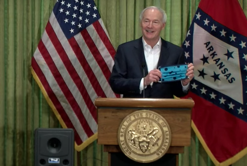 Arkansas Gov. Asa Hutchinson holds a mask Sunday during a briefing in Little Rock in this screen grab of video provided by the governor's office. 