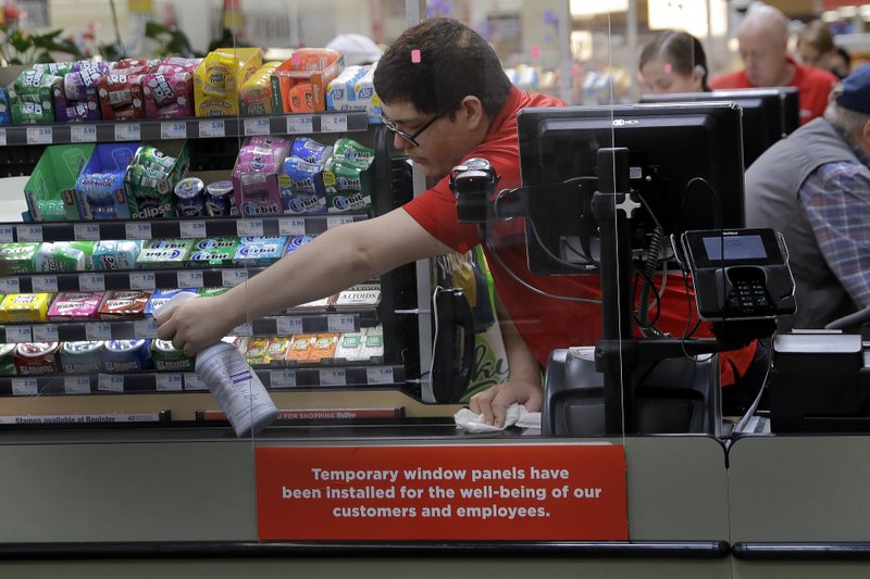 Garrett Ward sprays disinfectant on a conveyor belt between checking out shoppers behind a plexiglass panel on March 26 at a Hy-Vee grocery store in Overland Park, Kan. From South Africa to Italy to the U.S., grocery workers -- many in low-wage jobs -- are manning the front lines amid worldwide lockdowns, their work deemed essential to keep food and critical goods flowing. - AP Photo/Charlie Riedel