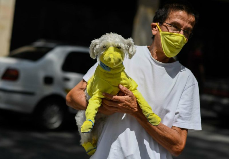 A man wears a face mask while he carries his dog with a protective suit as a preventive measure against the spread of the new coronavirus, covid-19, in Caracas, Venezuela, on March 20. People are worried about their pets, and doctors are advising precautions.

(AFP via Getty Images/TNS/Federico Parra)