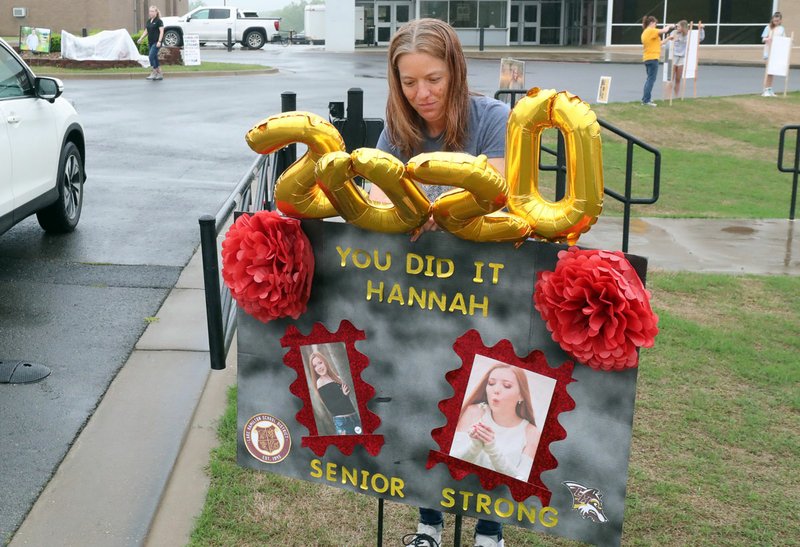 Chastity Bastien puts balloons on a sign congratulating her daughter, Hannah Kirk, on graduating from Lake Hamilton High School at the school Tuesday. Parents lined the road through the school to the drive-through pick-up area with signs congratulating the students. - Photo by Richard rasmussen of The Sentinel-Record