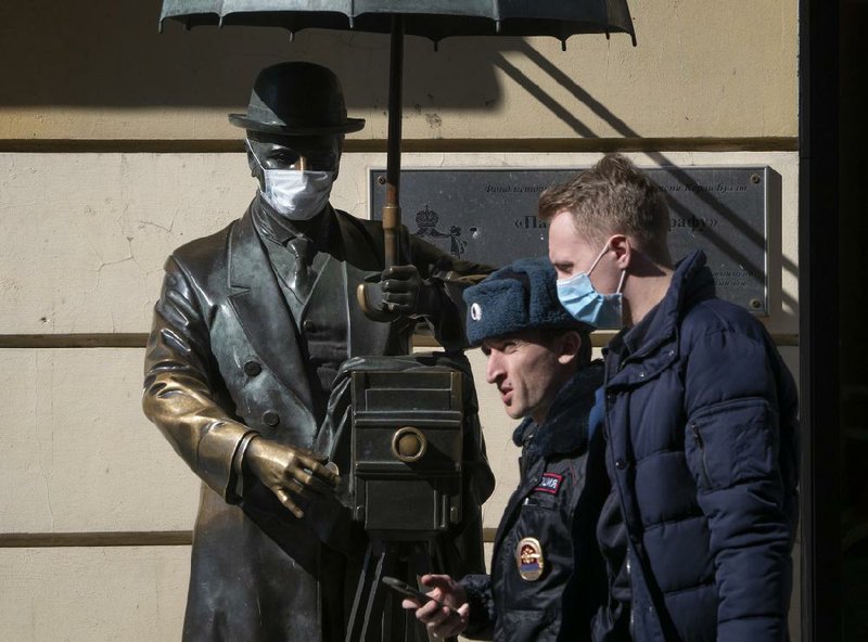 A police officer and another man walk past a statue wearing a face mask Tuesday in St. Petersburg, Russia. (AP/Dmitri Lovetsky) 