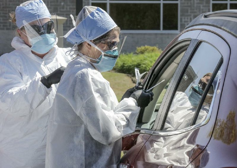 Registered nurses Amanda Velasquez (left) and Ursula Dixon take swabs from a couple in April 2020 at a drive-up coronavirus testing site at Arkansas Surgical Hospital in North Little Rock. (Arkansas Democrat-Gazette file photo)