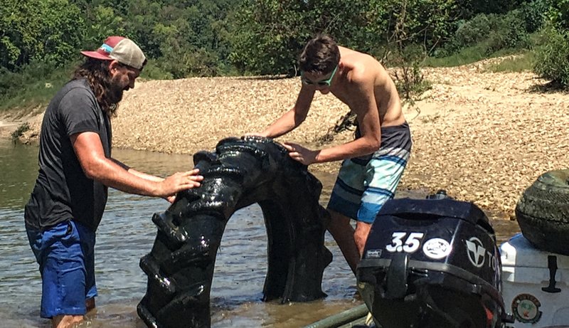 Michael Sacomani (left) and son Mason check out the tractor tire they found in the Saline River. the family spent its pandemic social distancing time in spring 2020 boating  the Saline River from their yard and hauling out trash.  (Special to the Democrat-Gazette/Michael and Tonya Sacomani)