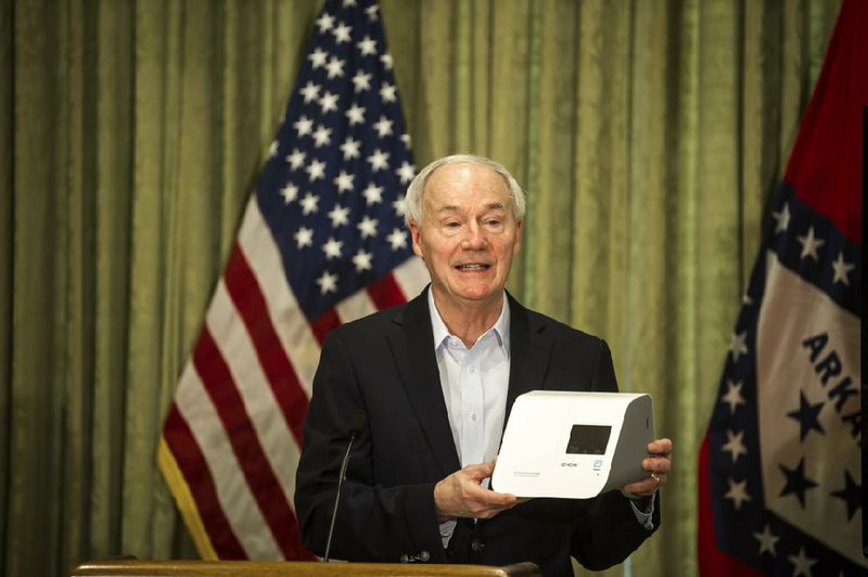 Gov. Asa Hutchinson holds a quick-testing device made by Abbott during Saturday’s news conference. The machine reportedly can provide covid-19 test results in about 15 minutes. More photos at arkansasonline.com/419gov/.
(Arkansas Democrat-Gazette/Stephen Swofford)