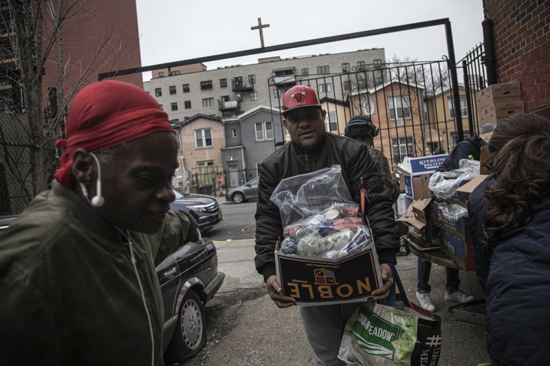Surrounded by a few volunteers, a man carries food donations from St. Stephen Outreach in the Brooklyn borough of New York, on Friday, March 20, 2020. For decades, American nonprofits have relied on a cadre of volunteers who quite suddenly aren't able to show up. With millions staying home during the pandemic, charities that help the country's neediest are facing even greater need. Many Americans have now been ordered to shelter in place, but there is an exception for people providing essential services, and that includes food bank volunteering. (AP Photo/Wong Maye-E)