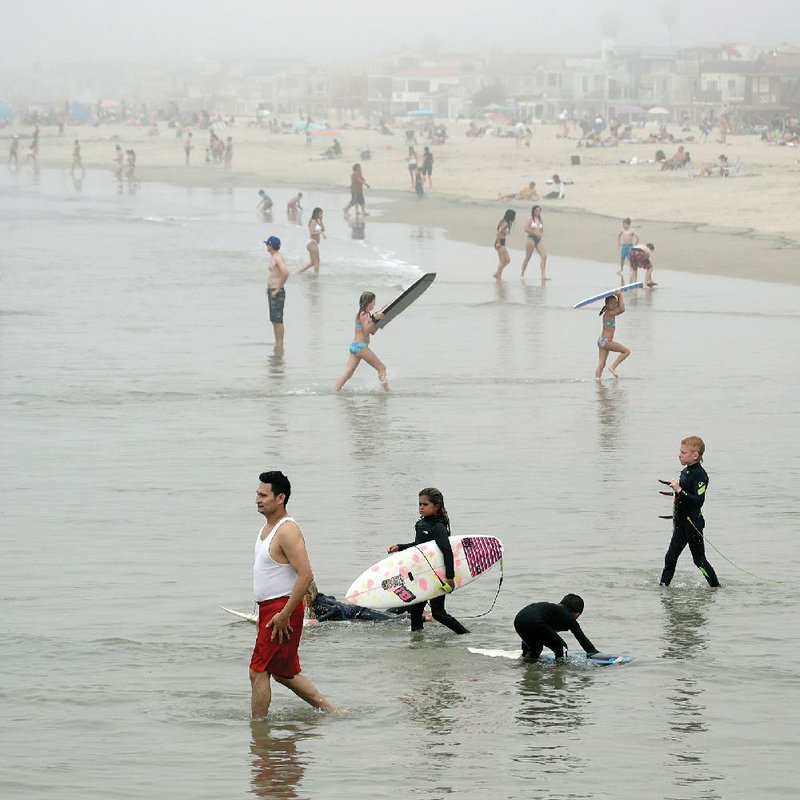 Swimmers and surfers take to the water Sunday in Newport Beach, Calif. A heat wave lured people to the beaches, leading officials to warn that defiance of stay-at-home orders could reverse progress against the coronavirus. More photos at arkansasonline.com/427covid/. (AP/Marcio Jose Sanchez) 