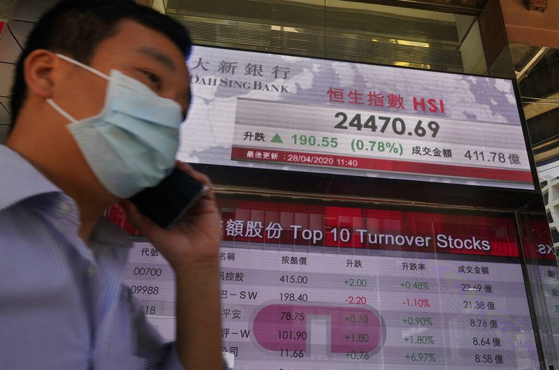 A man wearing a face mask walks past a bank electronic board showing the Hong Kong share index at Hong Kong Stock Exchange Tuesday, April 28, 2020.
