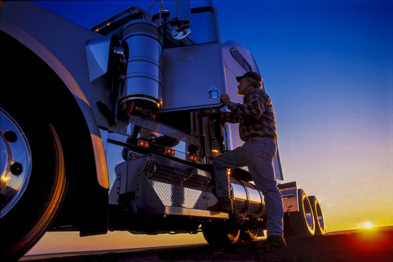 A stock photo shows a truck driver entering his rig. 