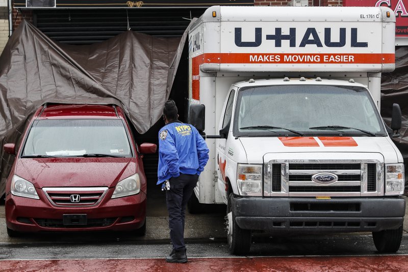 A NYPD officer walks up beside rental trucks and a hearse that have their back-ends covered by a tarp outside Andrew T. Cleckley Funeral Home, Thursday, April 30, 2020, in the Brooklyn borough of New York. Police were called to the funeral home Wednesday after it resorted to storing dozens of bodies on ice in rented trucks. The scene was the latest example of funeral homes struggling with thousands of deaths caused by the coronavirus. (AP Photo/John Minchillo)
