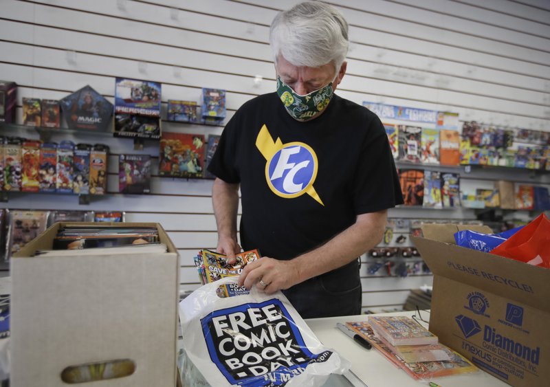 In this photo taken on Wednesday, April 29, 2020, Joe Feld, owner of Flying Color Comics, loads comics into plastic bags for curbside delivery outside his shop in Concord, Calif. The biggest day of the year for comics retailers in America is May 2, Free Comic Book Day, which Feld created. There will be no such day this May, and no comics to populate it after the main distributor stopped shipping product. Will the industry that fuels millions of collectors' superhero dreams and provides fodder for Hollywood's biggest blockbusters be dealt a powerful death blow by the effects of the coronavirus? (AP Photo/Ben Margot)