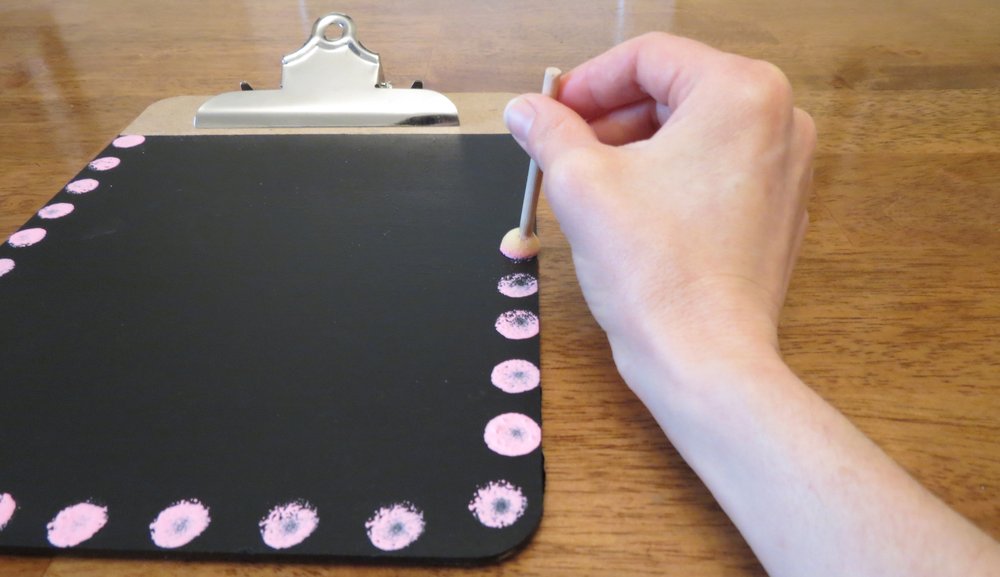 4. When the chalkboard is dry, peel off the blue tape. Squeeze more paint onto the paper plate, as before, then dab the round sponge brush into a color. Stamp the sides and bottom of the chalkboard. Rinse the sponge in water, then squeeze, before changing colors. Let dry for five minutes. (Photo for The Washington Post by Kris Coronado)