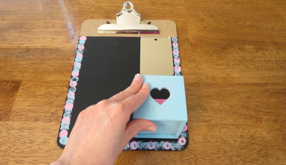 5. Keep the clipboard flat and glue the mirror to the top right of the chalkboard. (The glue doesnմ dry right away, so donմ tilt the clipboard!) Glue the painted box to the bottom right with the opening facing the top of the clipboard. (Photo for The Washington Post by Kris Coronado)