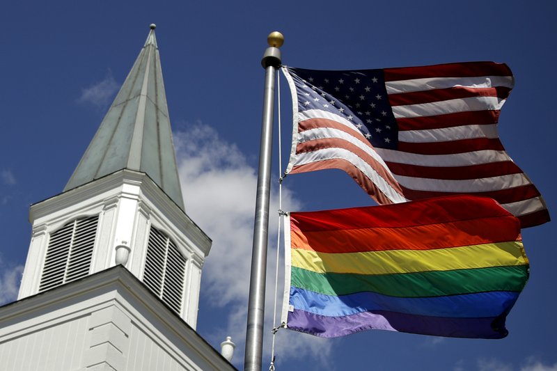 FILE - In this April 19, 2019 file photo, a gay pride rainbow flag flies along with the U.S. flag in front of the Asbury United Methodist Church in Prairie Village, Kan. Had there been no COVID-19 coronavirus pandemic, America&#x2019;s largest mainline Protestant denomination would be convening in May 2020 for a likely vote on breaking up over differences on same-sex marriage and ordination of LGBTQ pastors. (AP Photo/Charlie Riedel, File)