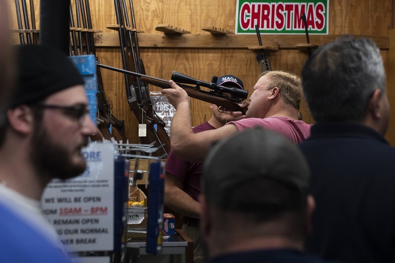 In this Friday, March 20, 2020, photo, a customer looks through a rifle scope as Bob's Little Sport Shop bustles with customers, in Glassboro, N.J. Gun retailers in New Jersey can remain open as essential businesses during the coronavirus outbreak. (Joe Lamberti/Camden Courier-Post via AP)