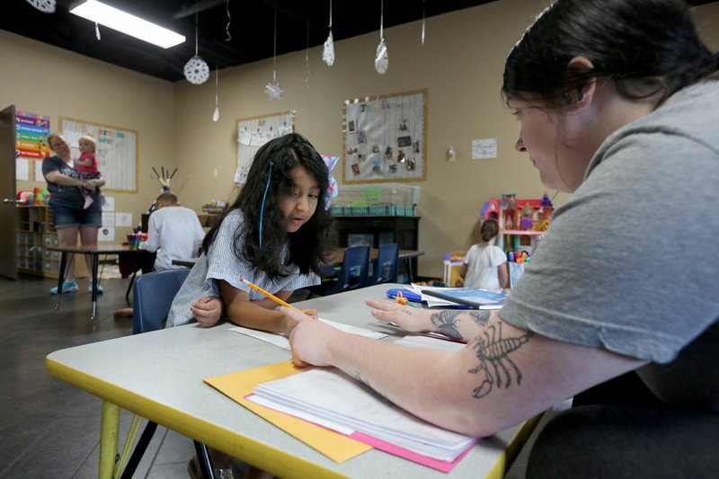 Serena Perry (right), a lead teacher at Butterflies &amp; Frogs Childcare and Preschool, helps Annie Mendoza-Guadian, 6, on her alternative method of instruction school work Tuesday at the Fayetteville center. Many of the center's students are children of front-line responders such as health care workers and children staying there is down by two-thirds, co-owner Greg Houser said Monday. Go to nwaonline.com/200506Daily/ and nwadg.com/photos for a photo gallery. (NWA Democrat-Gazette/David Gottschalk)
