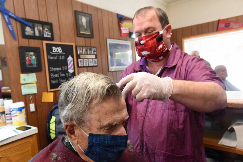 Bob Prince gives a haircut on Wednesday to Gerald Walsh (right) of Rogers at Bob's Barbershop in downtown Rogers. Barbershops, hair salons and tattoo businesses were allowed to open Wednesday with certain guidelines until further notice. Business is by appointment only. Stylists and customers are required to wear masks. Customers must wait outside for their appointment. Social distancing should be practiced when possible. Prince and barber Marty Pollock (left) reported brisk business Wednesday at the barbershop. Go to nwaonline.com/200507Daily/ to see more photos. (NWA Democrat-Gazette/Flip Putthoff)