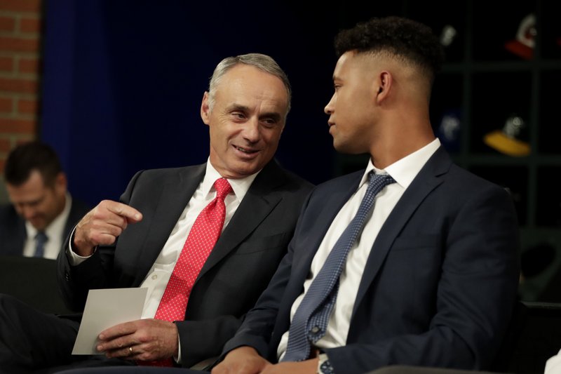 FILE - In this June 3, 2019, file photo, Major League Baseball Commissioner Rob Manfred, left, talks to Brennan Malone, a right-handed pitcher from IMG Academy in Bradenton, Fla., during the first round of the Major League Baseball draft in Secaucus, N.J. Major League Baseball will cuts its amateur draft from 40 rounds to five this year, a move that figures to save teams about $30 million. (AP Photo/Julio Cortez, File)