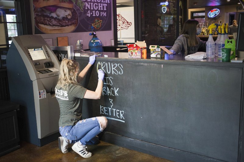 Server Madison Reynold writes a welcome message Monday at Grub's Bar and Grill in Rogers. Restaurants opened their doors with increased safety precautions Monday. They have spaced seating 10 feet apart and are operating at half of the building's capacity, said Jason Collins, the restaurant's co-owner. They require customers entering, going to the bathroom or exiting the building wear a mask. Go to nwaonline.com/200512Daily/ for today's photo gallery. (NWA Democrat-Gazette/Charlie Kaijo)