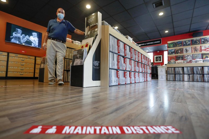 Mark Mawhinney walks past one of the racks of records towards the sticker on the floor reminding customers to maintain distances in his "Music to My Ears" retail record and HiFi store, Thursday, May 14, 2020, in Pittsburgh. He was preparing the store to re-open Friday when some of the COVID-19 restrictions will be lessened in Pittsburgh and several western Pennsylvania counties as they move from red to yellow status. (AP Photo/Keith Srakocic)