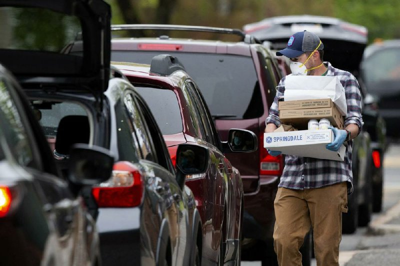 A Jack’s Abby craft brewery employee carries an order Friday to a customer in a line of cars waiting curbside in Framingham, Mass.
(AP/Michael Dwyer)
