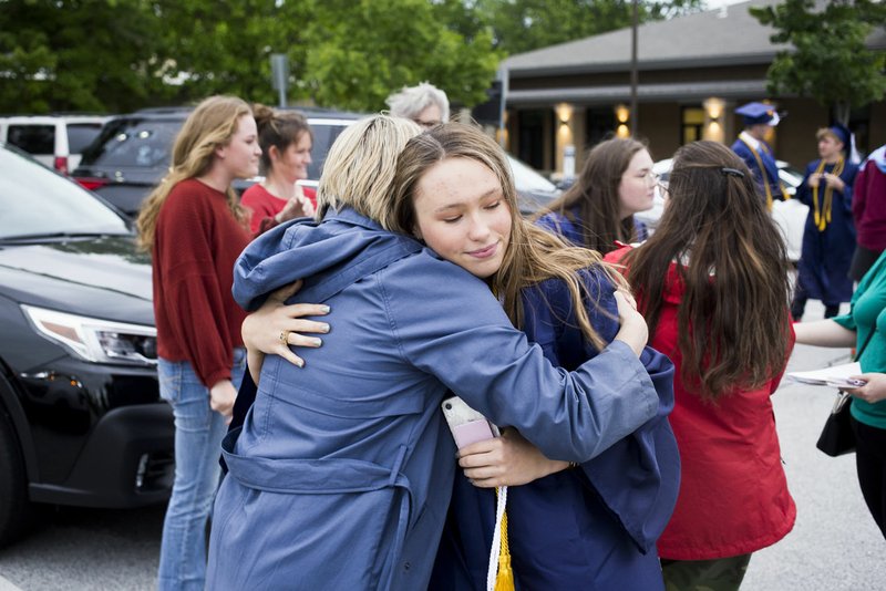 Kimberly Parker (from left) hugs daughter Cammie Parker on Friday during graduation at The New School in Fayetteville. The school celebrated its first graduation in a hybrid online/in-person ceremony. The senior class has of 11 students. The ceremony was outdoors where graduates and their families, the only guests in attendance outside of essential faculty and staff, were restricted to spaces within safe social distances to view recorded programming and to allow graduates to accept their diplomas one at a time. Go to nwaonline.com/200516Daily/ for today's photo gallery. (NWA Democrat-Gazette/Charlie Kaijo)