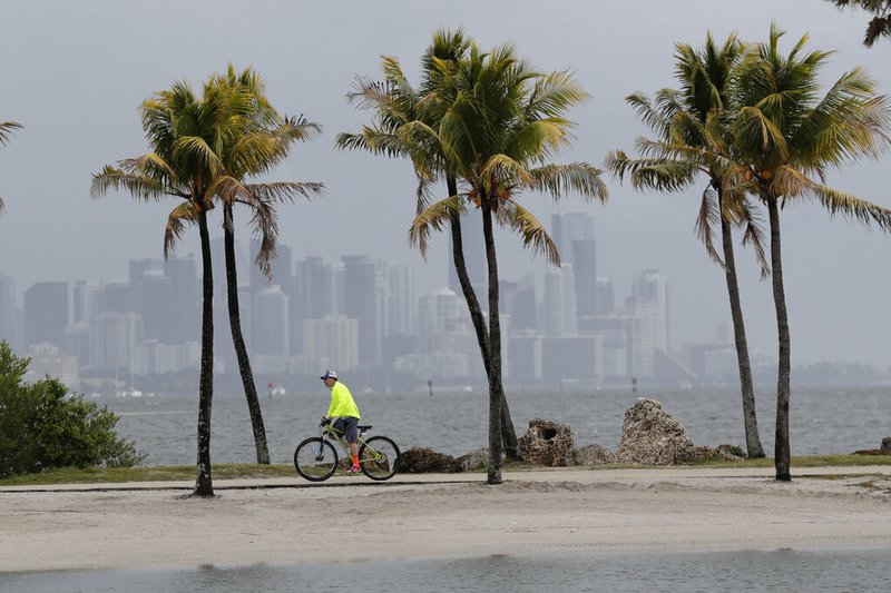 The Miami skyline is shrouded in clouds as a cyclist rides along Biscayne Bay at Matheson Hammock Park on Friday, May 15, 2020.