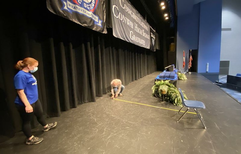 Lindsay Bradshaw, with Conway High School, watches as Ryan Tucker, a production team member with Conway Corp., marks off lines to set up the stage for the Conway High School virtual graduation set for broadcast on Sunday.
(Special to the Arkansas Democrat-Gazette)