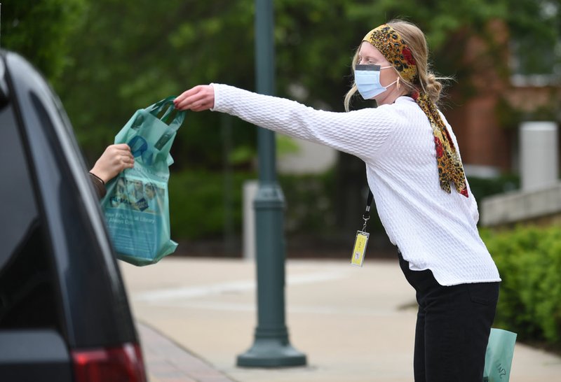 Erin Farrah with the Fayetteville Public Library brings out library materials for curbside pickup at the facility in downtown Fayetteville. (NWA Democrat-Gazette/David Gottschalk)