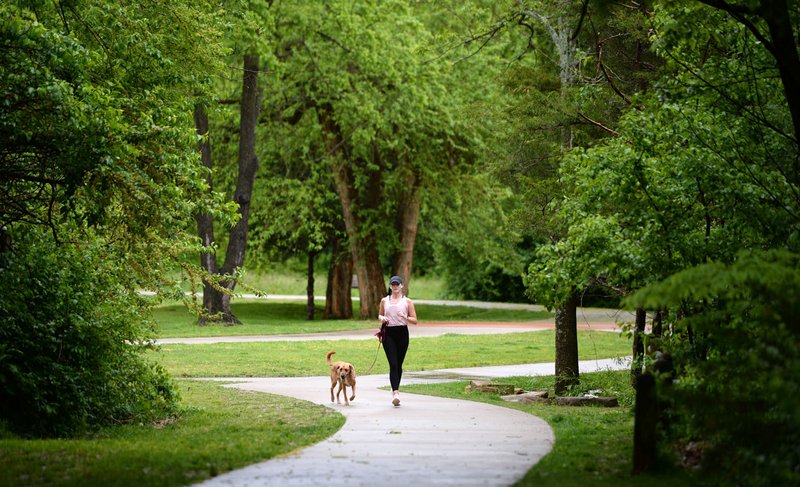 A resident walks alongside a dog Friday on the trail in Gulley Park in Fayetteville. The city has recorded a significant increase in trail users since the coronavirus pandemic hit in mid-March. The trail near Gulley Park has had a monthly average of about 25,000 users, compared to about 14,000 at the same time last year. Go to nwaonline.com/200518Daily/ for today's photo gallery. (NWA Democrat-Gazette/Andy Shupe)