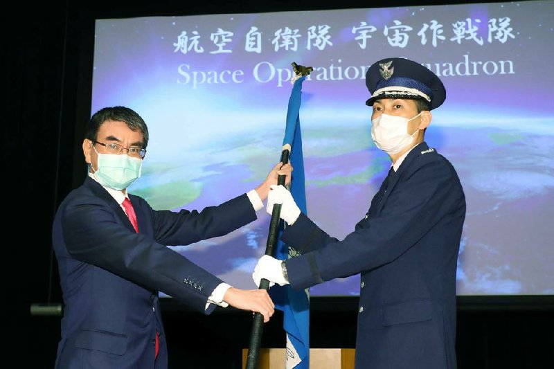 Japan Defense Minister Taro Kono, left, hands off a unit flag of the Space Operations Squadron to the head of the unit Toshihide Ashiki, right, at a launch ceremony at the Defense Ministry Monday, May 18, 2020, in Tokyo. The launch of the Space Operations Squadron reflects Japan's increasing need to defend itself from threats in cyberspace electromagnetic interference against Japanese satellites. (Kyodo News via AP)