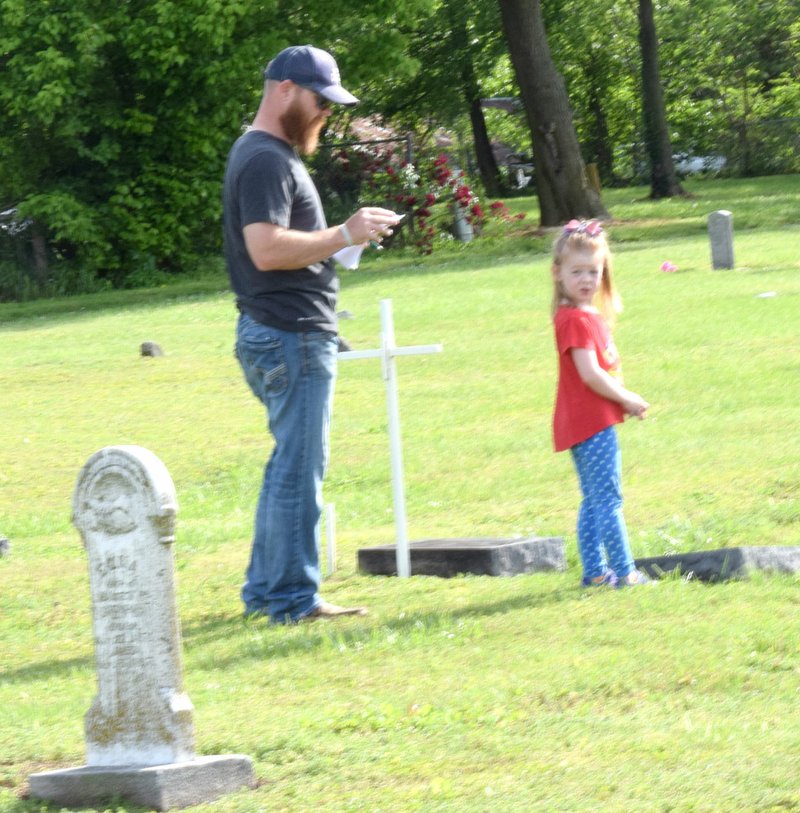 Westside Eagle Observer/MIKE ECKELS Matt McClain (left) and his daughter Magnolia work together to plant white crosses and flags on the graves of military veterans buried at Decatur Cemetery May 16. The crosses and flags were erected at the cemetery and along Decatur's two main thoroughfares to commemorate Memorial Day May 25.