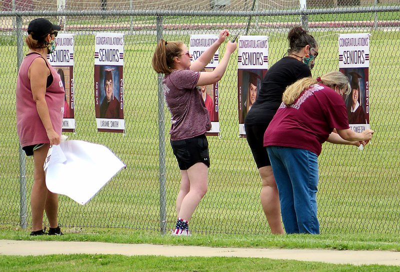 Westside Eagle Observer/RANDY MOLL Gentry High School teachers Alishia Ramsey (left), Erica Jones, Kristen Smartt and Toni Sarratt fasten banners with photos of 2020 graduates on the fence between the practice field and Pioneer Lane on Thursday. Banners to honor this year's graduates have also been placed on the Main Street light poles in downtown Gentry. A graduation date has been tentatively set for 6:30 p.m. on Friday, July 10, in Pioneer Stadium, with an alternate date of Saturday, July 11.