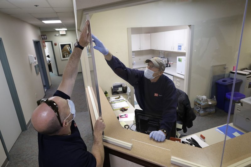 Crpenters John Mackie, of Canton, Mass., left, and Doug Hathaway, of Holliston, Mass., right, apply trim to a newly installed plastic barrier in an office area Wednesday at Boston University in Boston. Boston University is among a growing number of universities making plans to bring students back to campus this fall, but with new measures meant to keep the coronavirus at bay. - AP Photo/Steven Senne story.lead_photo.caption