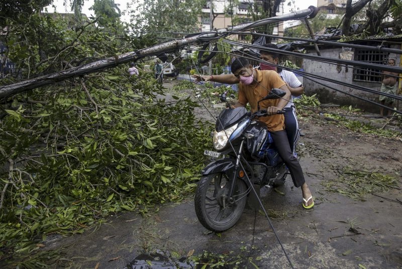 Motorists make their way through damaged cables and a tree branch fallen in the middle of a road after Cyclone Amphan hit the region in Kolkata, India, Thursday, May 21, 2020. People forgot about social distancing and crammed themselves into government shelters, minutes before Cyclone Amphan crashed in West Bengal.
(AP Photo/Bikas Das)