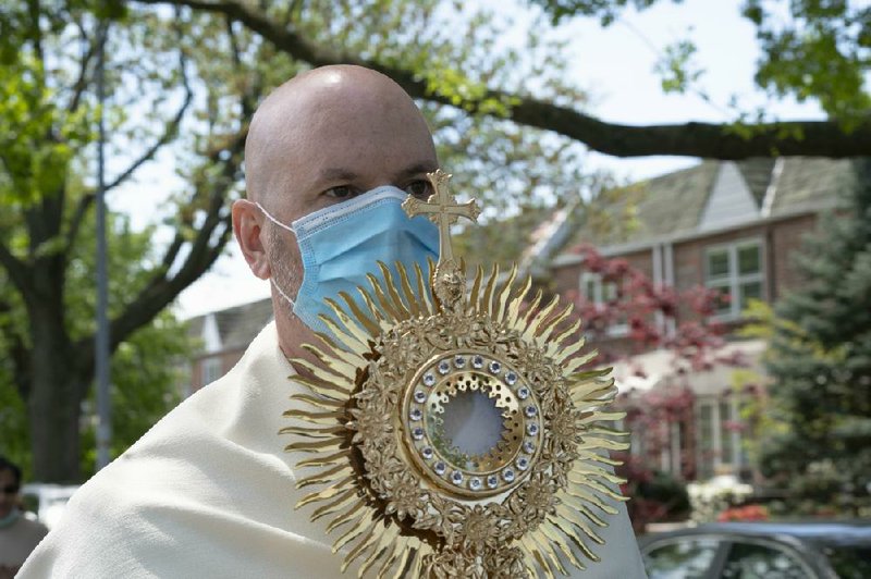 The Rev. Peter Purpura carries a monstrance during his procession in the Middle Village neighborhood of Queens on Sunday. After recovering from the coronavirus, Purpura found a way to bring the church directly to his people.
(The New York Times/James Estrin)