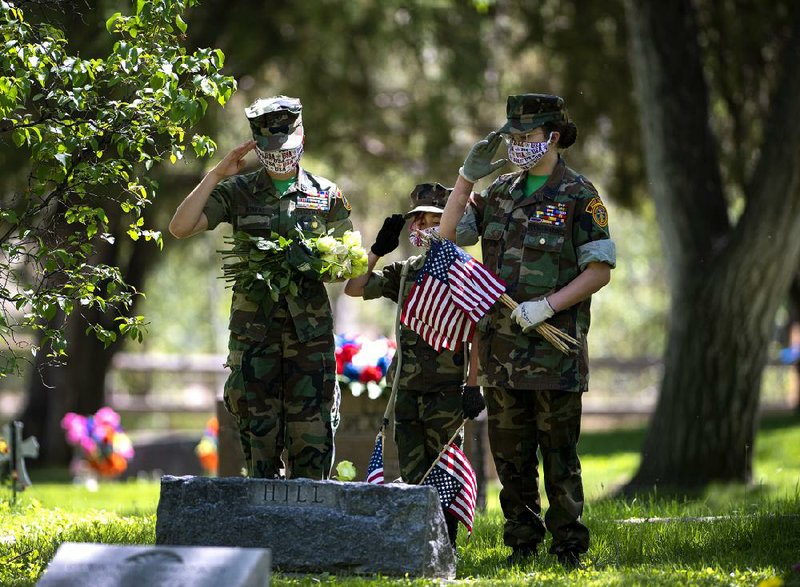 Members of the Pikes Peak Young Marines, Jhoanna Bonifas (left), 14, Riley Landis, 9, and Jessica Bonifas, 12, salute the grave of a veteran Friday at a cemetery in Fountain, Colo., as they help place flags and flowers on about 160 graves.
(AP/The Gazette/Christian Murdock)
