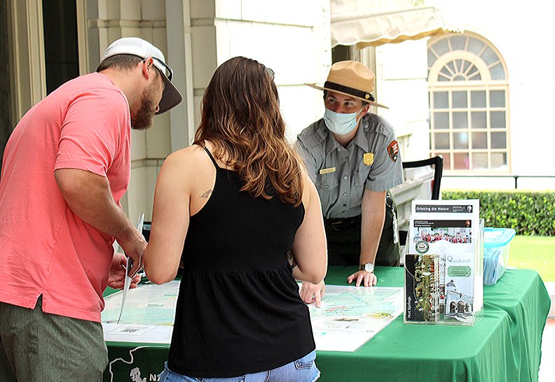 Hot Springs National Park Ranger Katy Foster shows two visitors a map of trails from the porch of the Fordyce Bath House on Saturday. Foster said that by noon on Saturday she had counted a few hundred visitors on the porch. On Friday, around 500 people visited the porch. - Photo by Tanner Newton of The Sentinel-Record