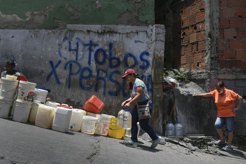 FILE - In this May 9, 2020, file photo, a woman carries containers of water in the Petare neighborhood, one of the poorest slums in Caracas, Venezuela, during a government-imposed quarantine to help stop the spread of the coronavirus. For people around the world who are affected by war and poverty, the simple act of washing hands is a luxury. (AP Photo/Matias Delacroix)