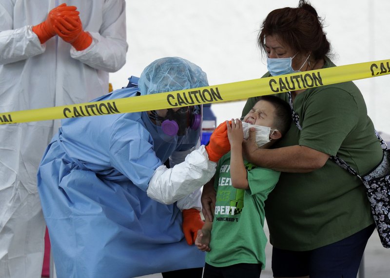 FILE - In this May 14, 2020, file photo, Jerry A Mann, center, is held by his grandmother, Sylvia Rubio, as he is tested for COVID-19 by the San Antonio Fire Department at a free walk-up test site in San Antonio. Public health officials have said robust testing for the coronavirus is essential to safely lifting stay-at-home orders and business closures, but states are creating confusion in the way they are reporting the data. (AP Photo/Eric Gay, File)