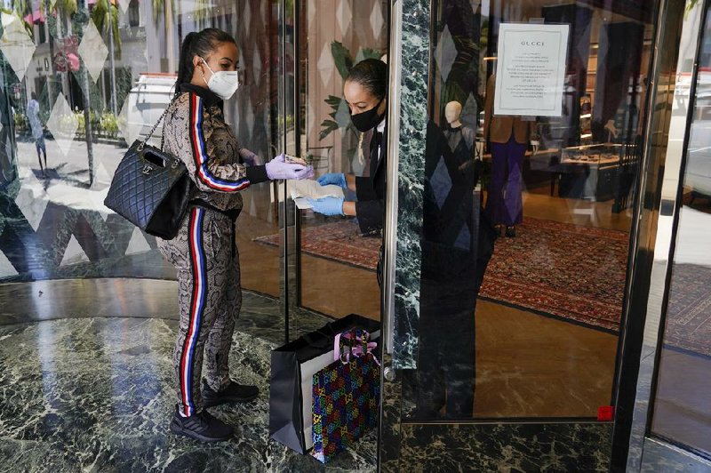 Delicia Cordon receives a purchase from a sales person at Gucci on Rodeo Drive on Tuesday in Beverly Hills, Calif. The store is closed for in-store shopping but offers curbside pickup for orders in advance. (AP/Ashley Landis) 