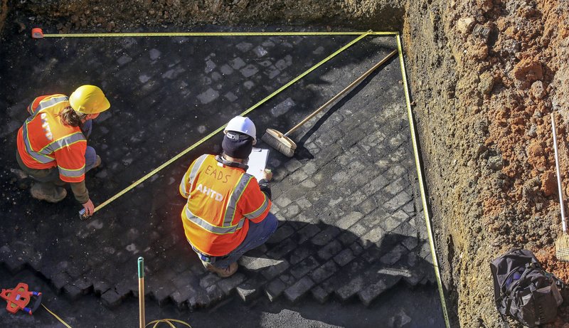 Archeaologists for the Arkansas Highway and Transportation Department Kristina Boykin (left) and Jason Eads in December 2016 measure a section of wood block pavers discovered underground while building the current Broadway Bridge. (Democrat-Gazette file photo)