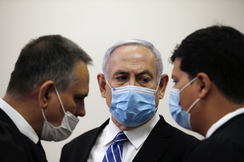 Israeli Prime Minister Benjamin Netanyahu, wearing a face mask in line with public health restrictions due to the coronavirus pandemic, looks at his lawyer inside the court room as his corruption trial opens at the Jerusalem District Court on Sunday. He is the country's first sitting prime minister ever to go on trial, facing charges of fraud, breach of trust, and accepting bribes in a series of corruption cases stemming from ties to wealthy friends. - Ronen Zvulun/ Pool Photo via AP