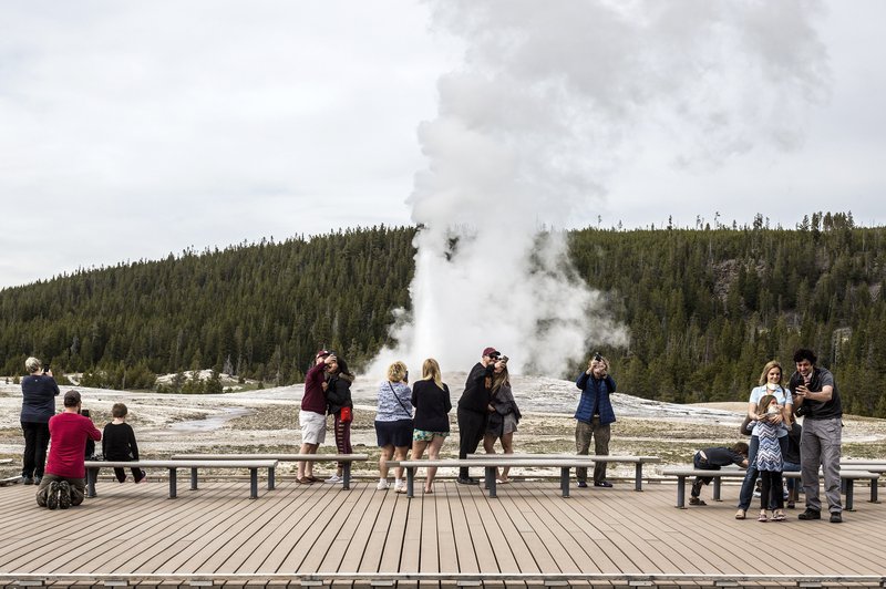 In this Monday, May 18, 2020 photo, visitors watch as Old Faithful erupts on the day the park partially reopened after a two-month shutdown due to the coronavirus pandemic, at Yellowstone National Park, Wyo. Officials at Yellowstone and other national parks plan to let tourists mostly police themselves and not intervene much to enforce social distancing. (Ryan Dorgan/Jackson Hole News &amp; Guide via AP)