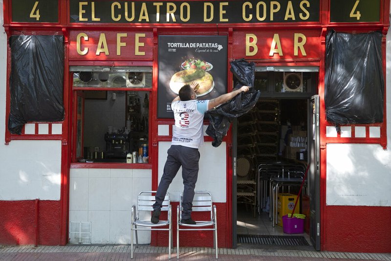 A worker uncovers the front of a bar ready to open for the first time in over two months in Madrid, Spain, Monday, May 25, 2020. Spain is making progress on its staggered plan out of the confinement against the coronavirus. Roughly half of the population, including residents in the biggest cities of Madrid and Barcelona, on Monday entered phase 1, which allows for social gatherings in limited numbers, restaurant and bar services with outdoor sitting and some cultural and sports activities.