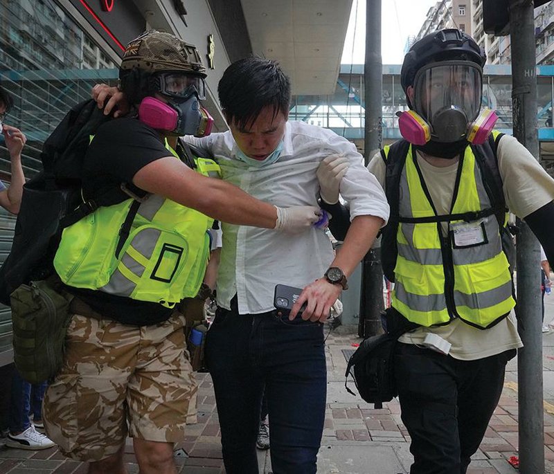 Medical volunteers help a man walk away from a shopping district in Hong Kong on Sunday as police fire tear gas during a protest against China’s national security legislation. More photos at arkan- sasonline.com/525hongkong/. 
(AP/Vincent Yu) 
