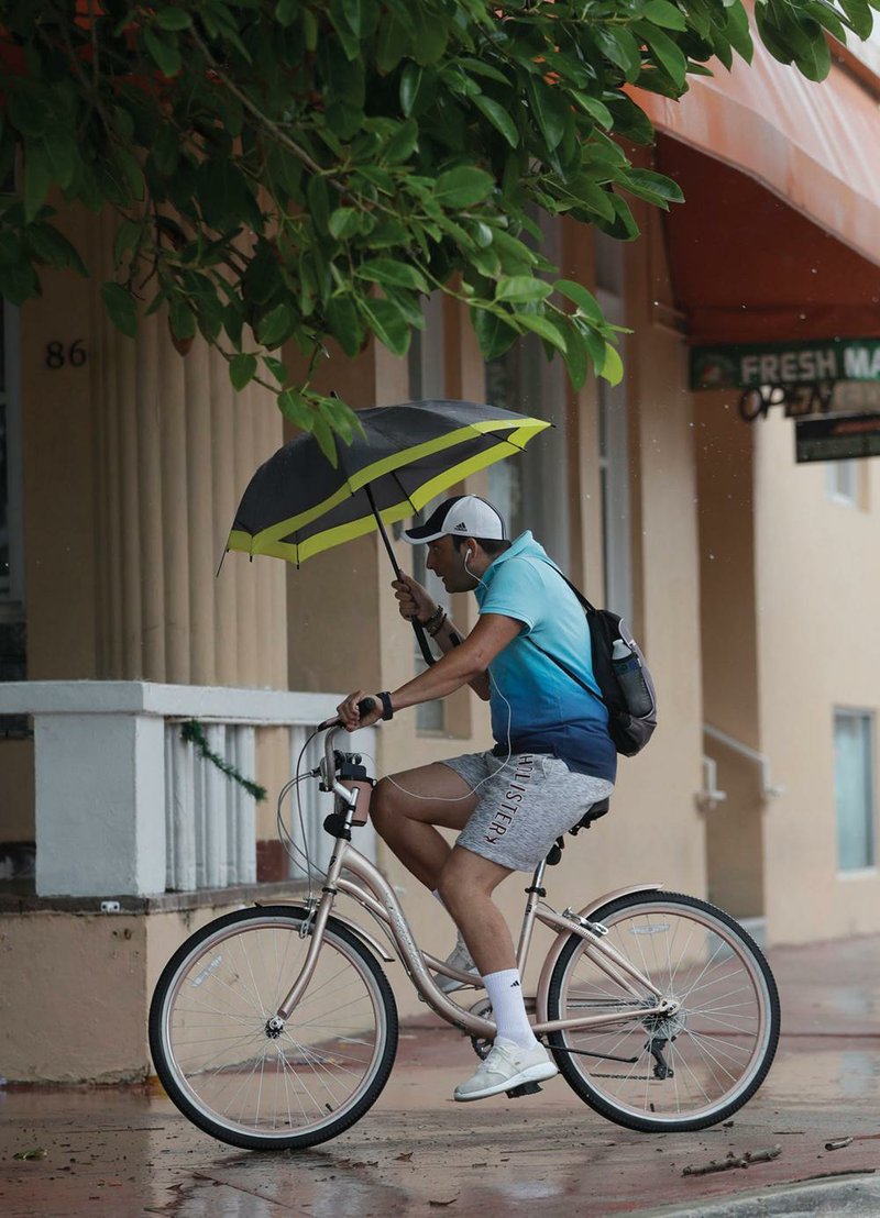 A man tries to take cover under an umbrella Monday as he rides along Ocean Drive in Miami Beach, Fla. (AP/Wilfredo Lee) 
