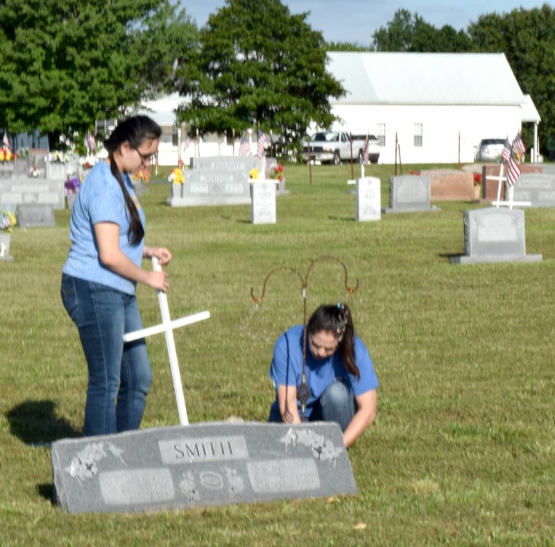 Westside Eagle Observer/MIKE ECKELS While Martha Smith-Gomez (left) waits to plant a white cross, Jacque Smith places a piece of pipe into the ground during the Falling Springs Cemetery work afternoon May 20 near Decatur. Ten volunteers placed 72 crosses on veterans' graves at Falling Springs in observance of Memorial Day, May 25.