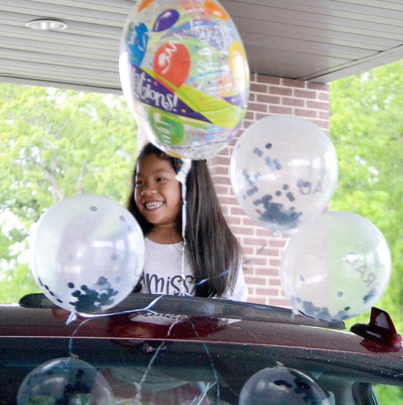 TIMES photographs by Annette Beard Grinning and surrounded by balloons, graduating kindergarten student Rosalie Allen shared flowers with teachers and staff during the drive-through kindergarten graduation Friday, May 22, 2020. Although kindergarten students have traditionally had a walk-through graduation ceremony in the high school gym, this year's was unusual and unique due to the restrictions imposed by state officials during the covid-19 pandemic. See more photographs online at tnebc.nwaonline.com/photos.